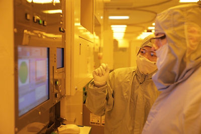 Two technicians in full body electronic PPE looking at a screen on lithography equipment.